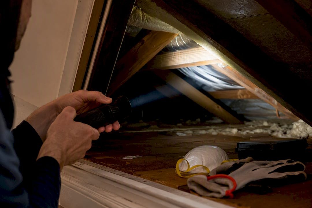 Hands shining flashlight into attic hatch