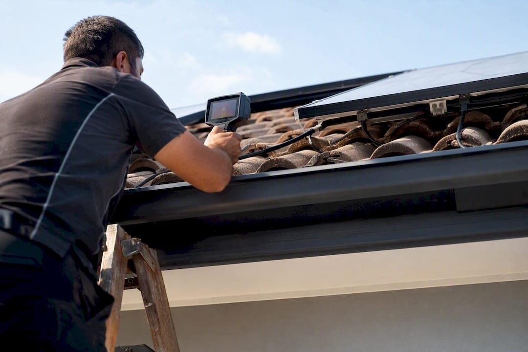 Technician using thermal camera on roof near solar panel wiring